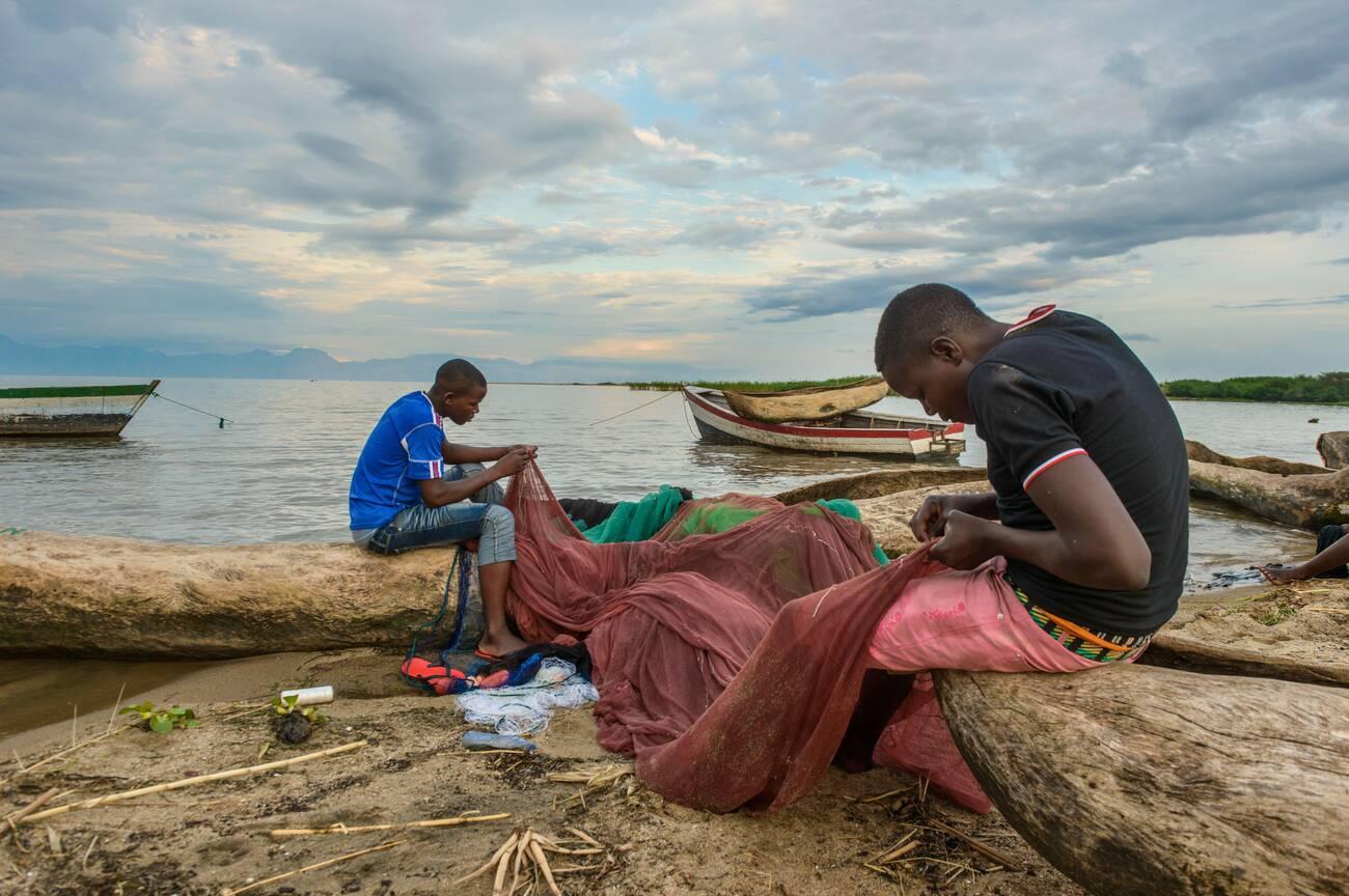 alamy_2B11889 Two fishermen mend their nets at a fish market on Lake Malawi, Malawi, Africa