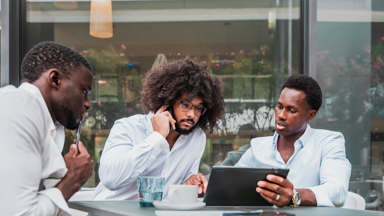 Young African professionals collaborating in a modern tech hub, working on laptops, startup office environment, bright natural lighting, innovative workspace, teamwork and collaboration concept